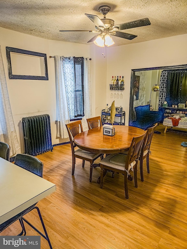 dining space with wood-type flooring, radiator heating unit, ceiling fan, and a textured ceiling