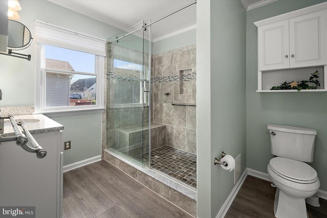 bathroom with toilet, wood-type flooring, ornamental molding, vanity, and a shower with door