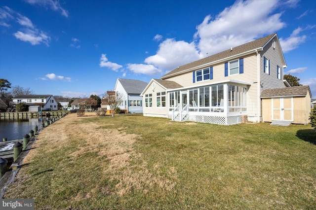 rear view of property featuring a sunroom, a storage shed, a lawn, and a water view