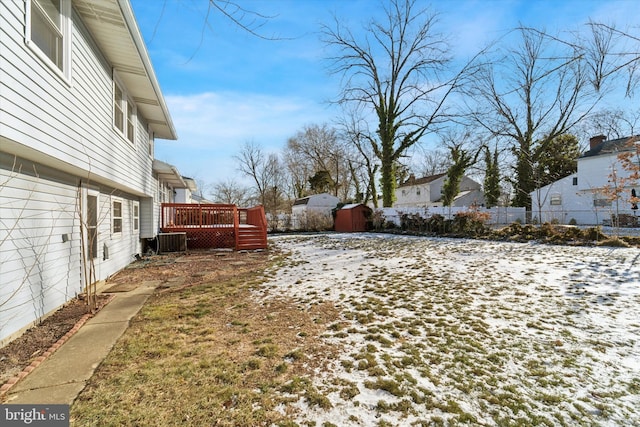 yard covered in snow featuring cooling unit, a shed, and a wooden deck