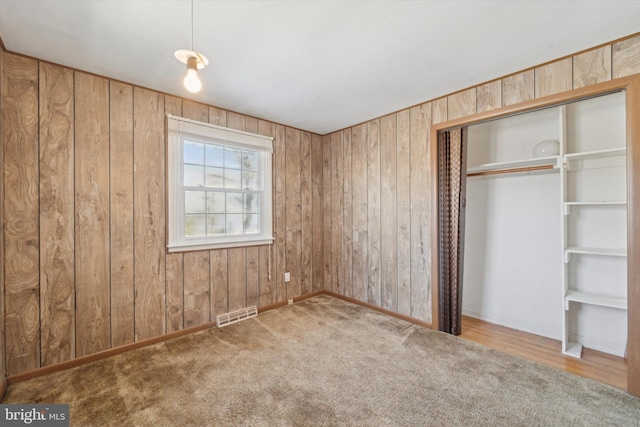 unfurnished bedroom with a closet, carpet floors, and wood walls