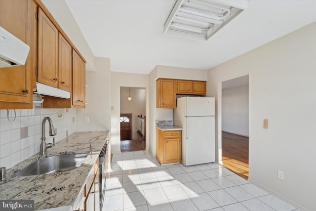 kitchen with light stone counters, dishwasher, white fridge, light tile patterned floors, and sink