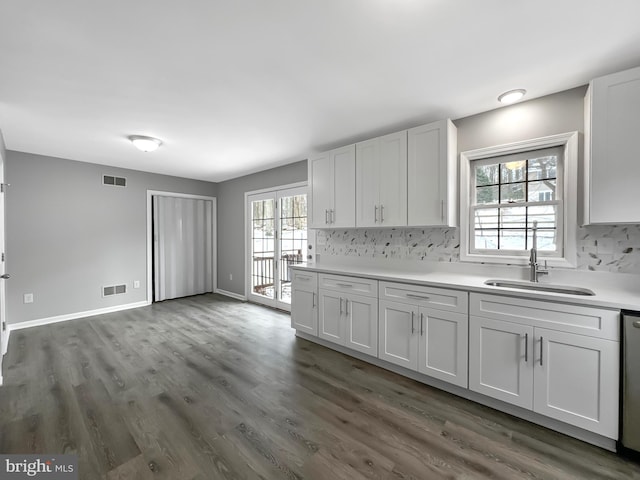 kitchen featuring dark wood-type flooring, stainless steel dishwasher, tasteful backsplash, white cabinetry, and sink