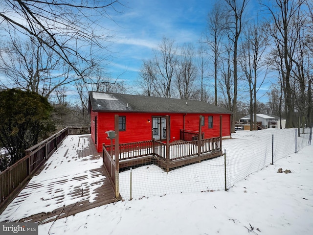 snow covered rear of property featuring a fenced backyard, a shingled roof, and a deck