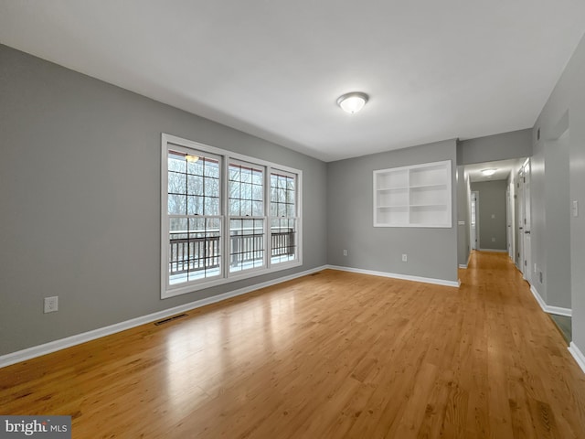 spare room featuring light wood-type flooring and built in shelves