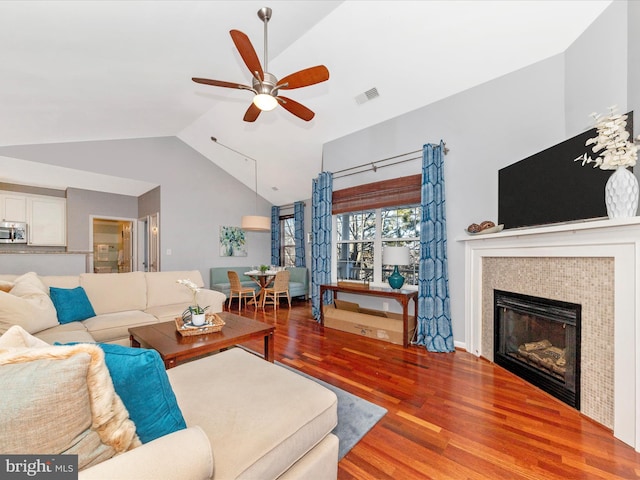 living room featuring hardwood / wood-style floors, vaulted ceiling, a tile fireplace, and ceiling fan