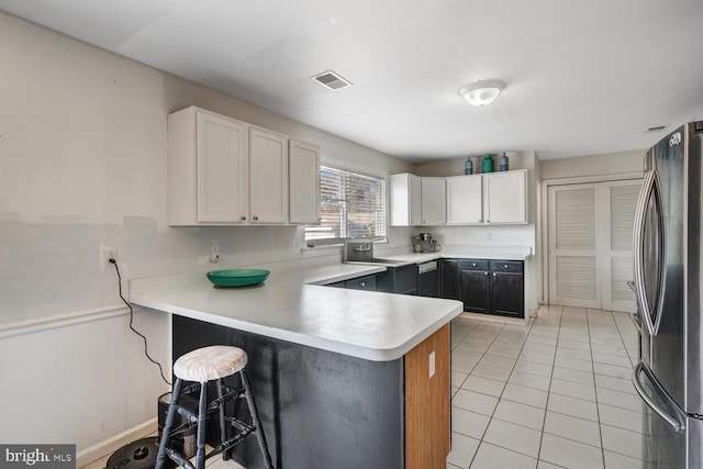 kitchen featuring kitchen peninsula, light tile patterned floors, white cabinetry, stainless steel refrigerator, and sink