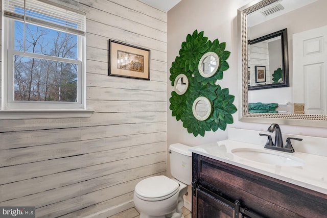 bathroom with toilet, vanity, and wood walls