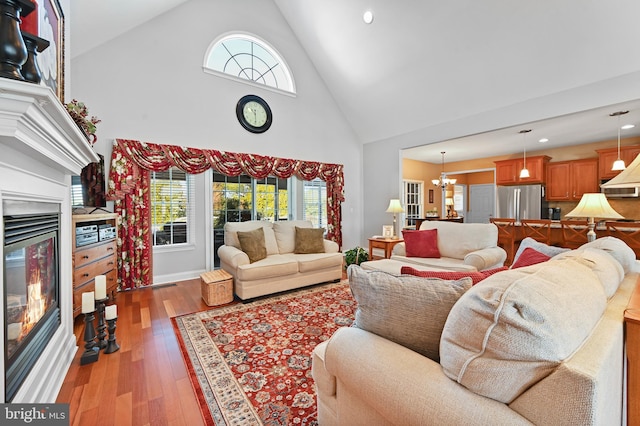 living room featuring high vaulted ceiling, a wealth of natural light, a notable chandelier, and light wood-type flooring