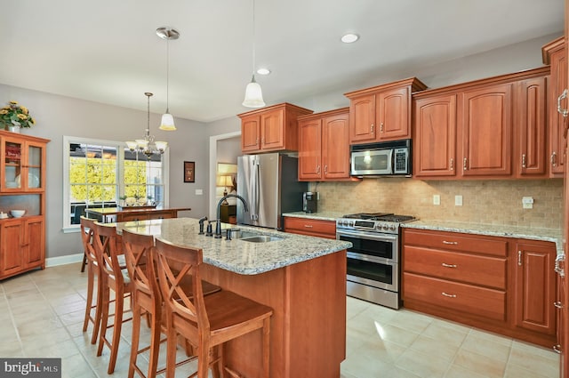 kitchen with light stone countertops, pendant lighting, appliances with stainless steel finishes, an island with sink, and an inviting chandelier