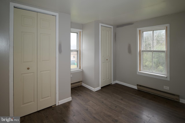 unfurnished bedroom with multiple windows, dark hardwood / wood-style flooring, and a baseboard radiator