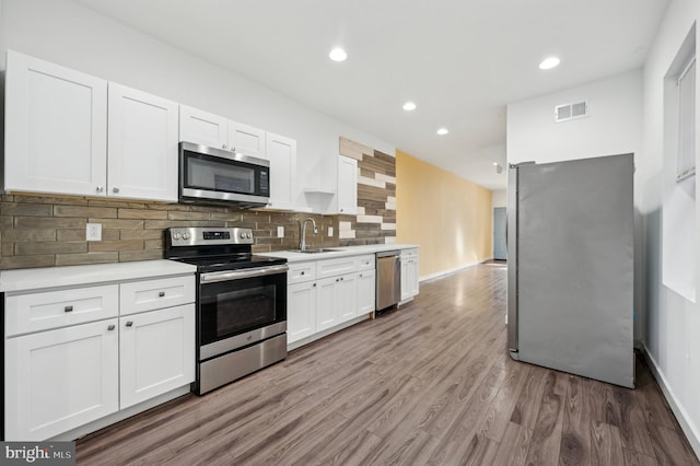 kitchen featuring sink, hardwood / wood-style flooring, stainless steel appliances, decorative backsplash, and white cabinets