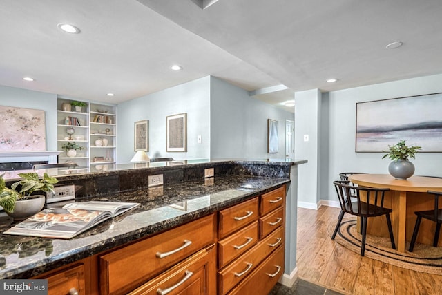 kitchen with hardwood / wood-style flooring, dark stone counters, and built in features