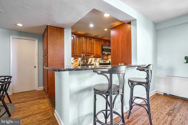 kitchen with a breakfast bar, light hardwood / wood-style floors, kitchen peninsula, and appliances with stainless steel finishes