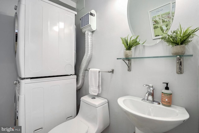 bathroom with sink, stacked washer / drying machine, and toilet