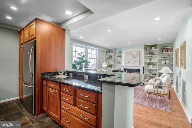 kitchen featuring kitchen peninsula, built in shelves, dark stone counters, and stainless steel fridge