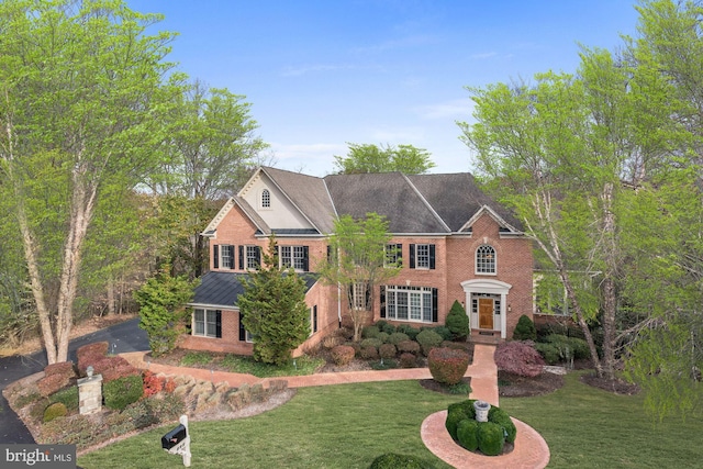 colonial inspired home with driveway, brick siding, and a front lawn