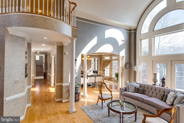 living area featuring light wood-style flooring, ornamental molding, a towering ceiling, and ornate columns