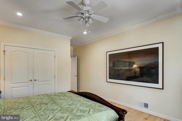 bedroom with visible vents, wood finished floors, a closet, crown molding, and baseboards