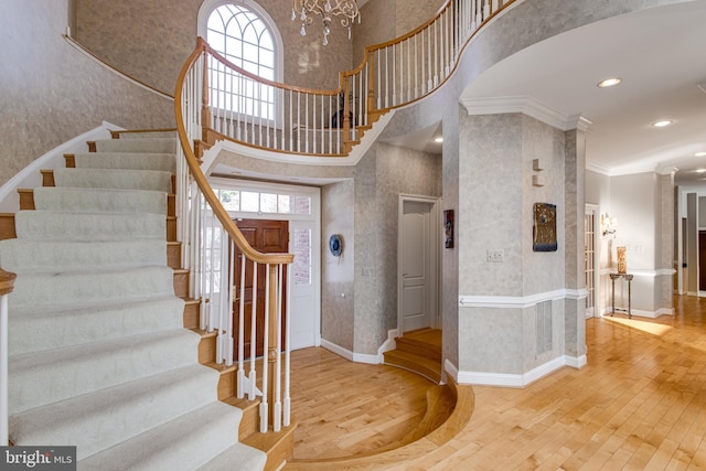 stairs with hardwood / wood-style floors, baseboards, wallpapered walls, a towering ceiling, and crown molding