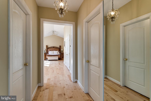 hallway with baseboards, an inviting chandelier, light wood-style flooring, and vaulted ceiling