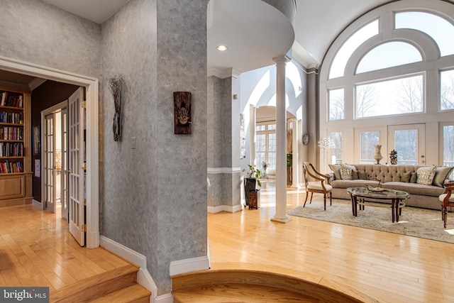 interior space with french doors, wood-type flooring, a towering ceiling, and decorative columns