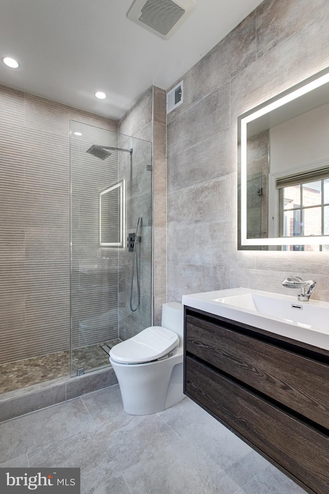 full bathroom with a tile shower, visible vents, toilet, and tile walls