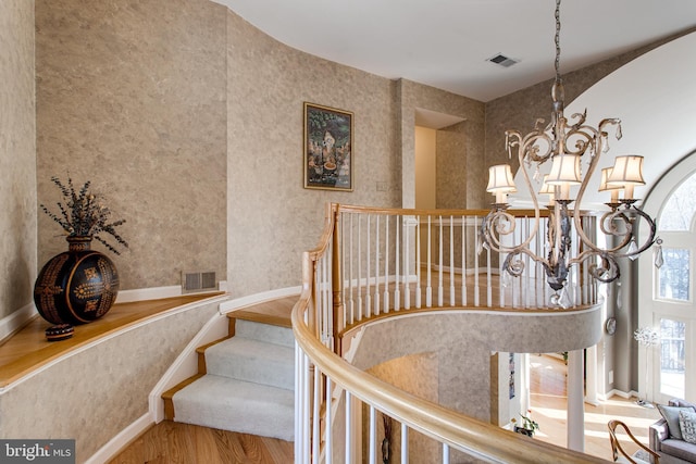 stairway with visible vents, a notable chandelier, wood finished floors, and wallpapered walls