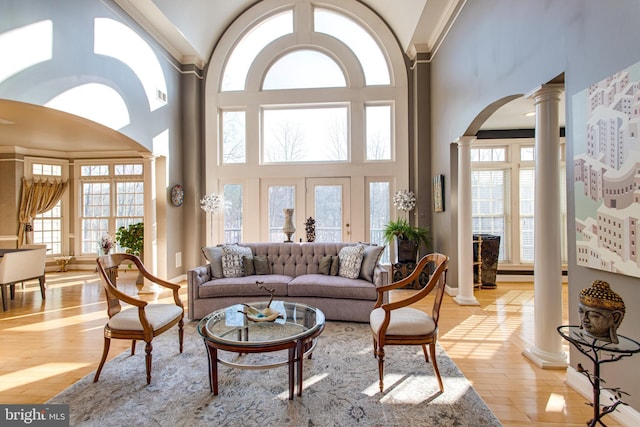 living room featuring baseboards, crown molding, light wood-style floors, and decorative columns