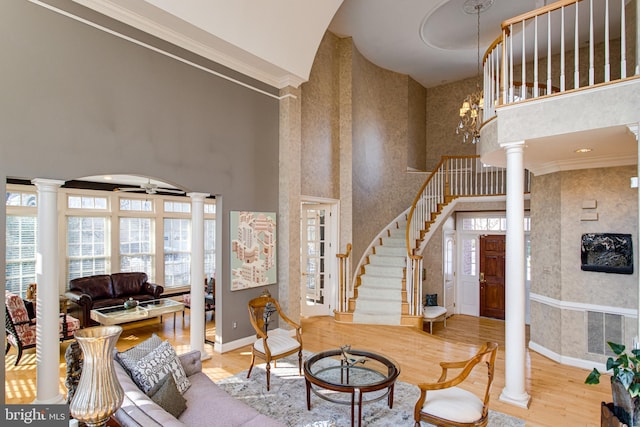 living room featuring a towering ceiling, wallpapered walls, ornate columns, and wood finished floors