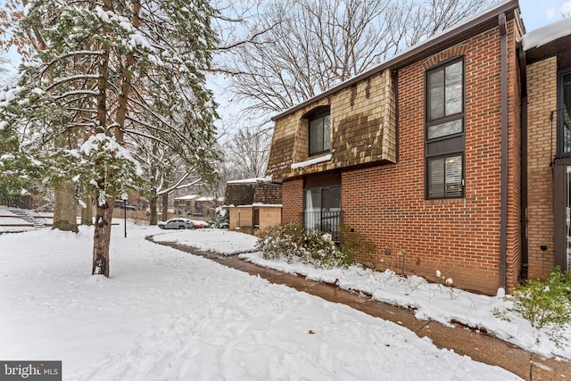 view of snowy exterior featuring brick siding and mansard roof