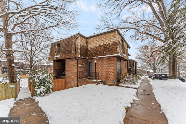 snow covered property featuring brick siding, fence, and mansard roof