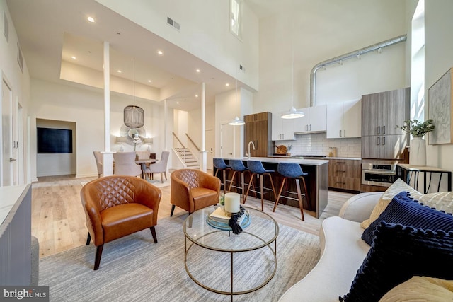 living room with a towering ceiling, sink, and light hardwood / wood-style floors