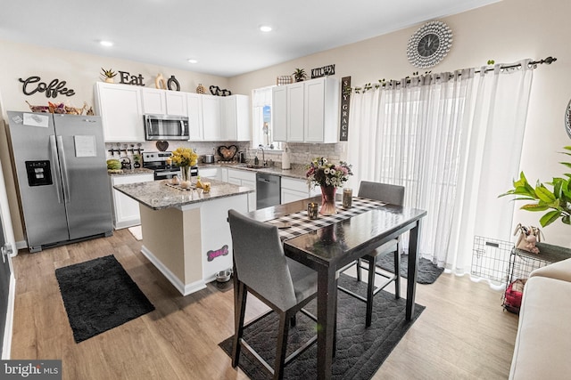 kitchen with appliances with stainless steel finishes, a center island, light stone countertops, white cabinetry, and backsplash