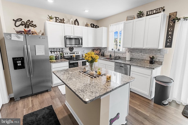 kitchen featuring stainless steel appliances, sink, white cabinets, a center island, and light stone countertops