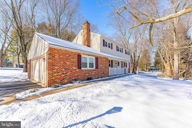 snow covered property featuring covered porch and a garage