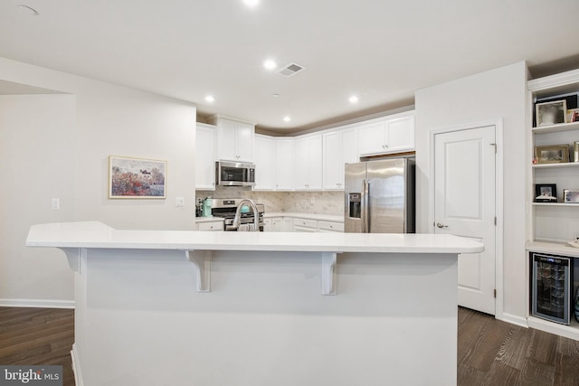 kitchen with a large island with sink, appliances with stainless steel finishes, beverage cooler, and a breakfast bar area