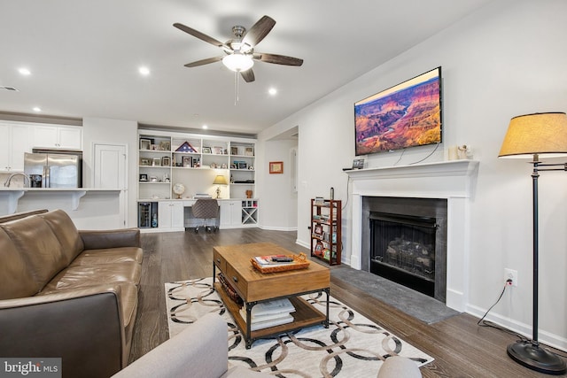 living room with ceiling fan, dark hardwood / wood-style flooring, built in desk, and built in shelves