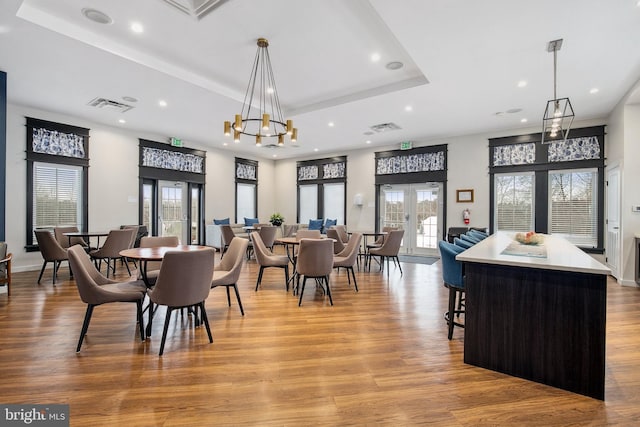 dining space with light wood-type flooring, a healthy amount of sunlight, french doors, and a tray ceiling