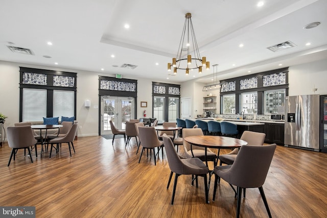 dining room with light wood-type flooring, a healthy amount of sunlight, french doors, and a tray ceiling