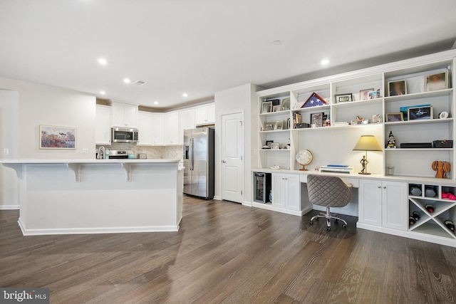 kitchen with white cabinets, a breakfast bar, stainless steel appliances, and built in desk