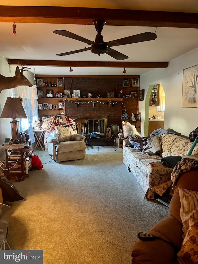 living room with ceiling fan, a brick fireplace, carpet floors, and beamed ceiling