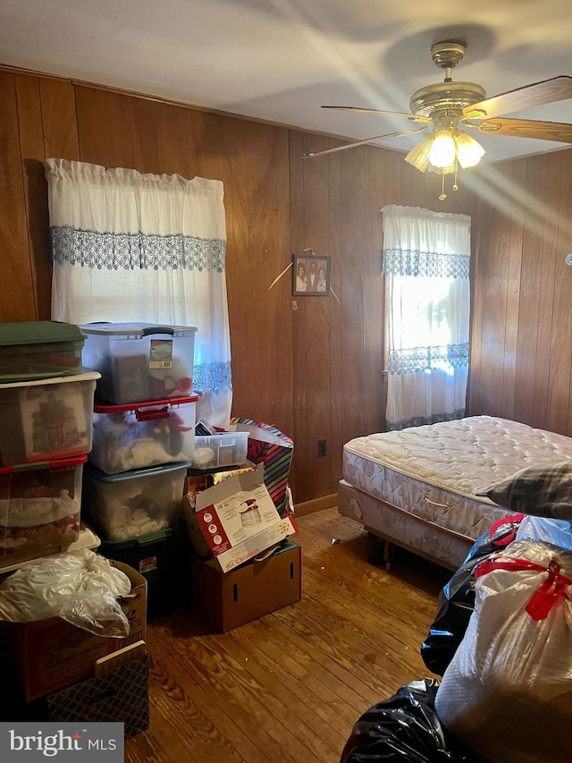 bedroom with wood-type flooring, wooden walls, and ceiling fan