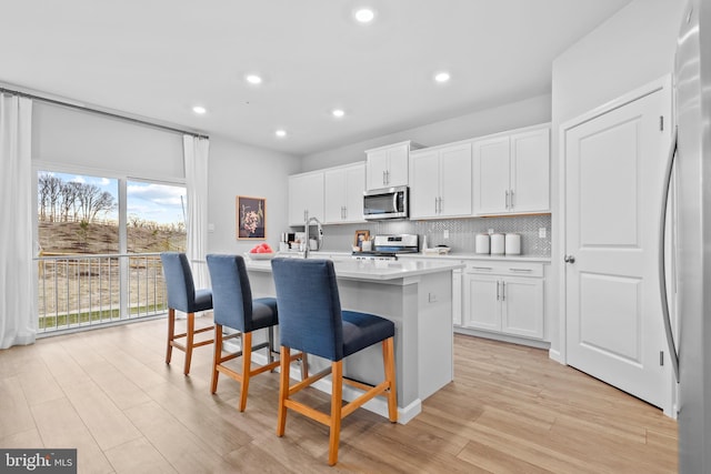 kitchen with white cabinets, stainless steel appliances, an island with sink, and a breakfast bar area