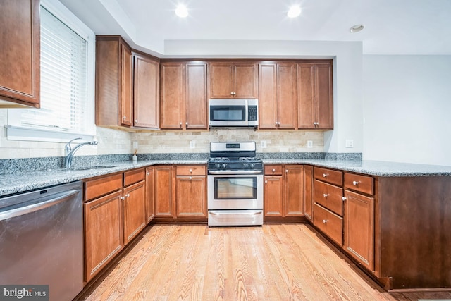 kitchen featuring stone countertops, appliances with stainless steel finishes, sink, light wood-type flooring, and decorative backsplash