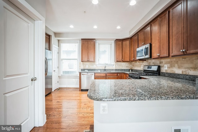 kitchen featuring stainless steel appliances, dark stone counters, sink, kitchen peninsula, and light hardwood / wood-style flooring