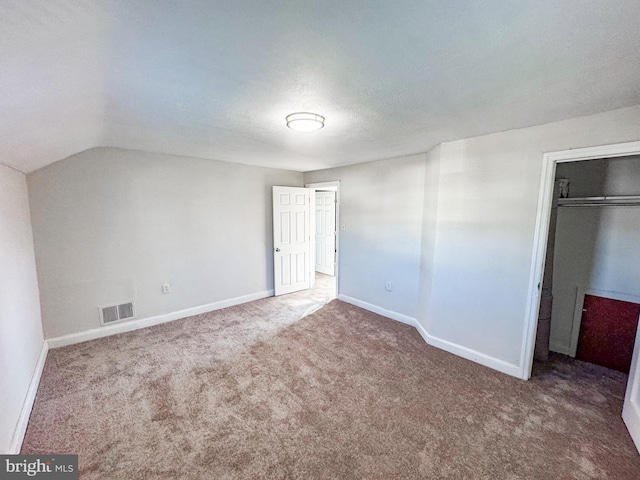 unfurnished bedroom with vaulted ceiling, a textured ceiling, carpet floors, and a closet