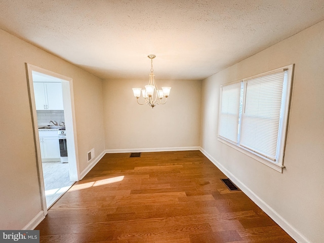 unfurnished dining area featuring hardwood / wood-style flooring, a textured ceiling, a notable chandelier, and sink