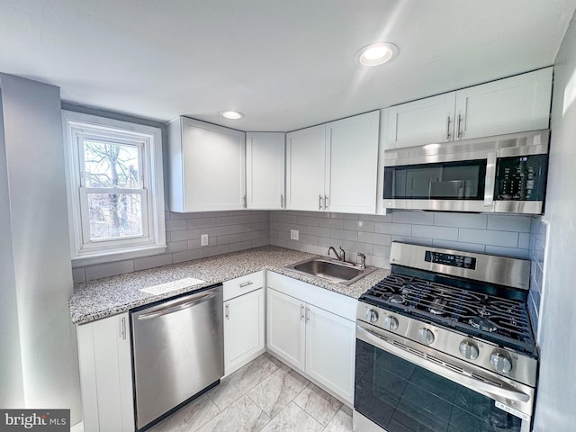 kitchen with light stone counters, decorative backsplash, white cabinets, appliances with stainless steel finishes, and sink