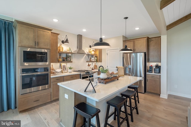 kitchen featuring appliances with stainless steel finishes, light wood-type flooring, a center island with sink, island range hood, and beam ceiling